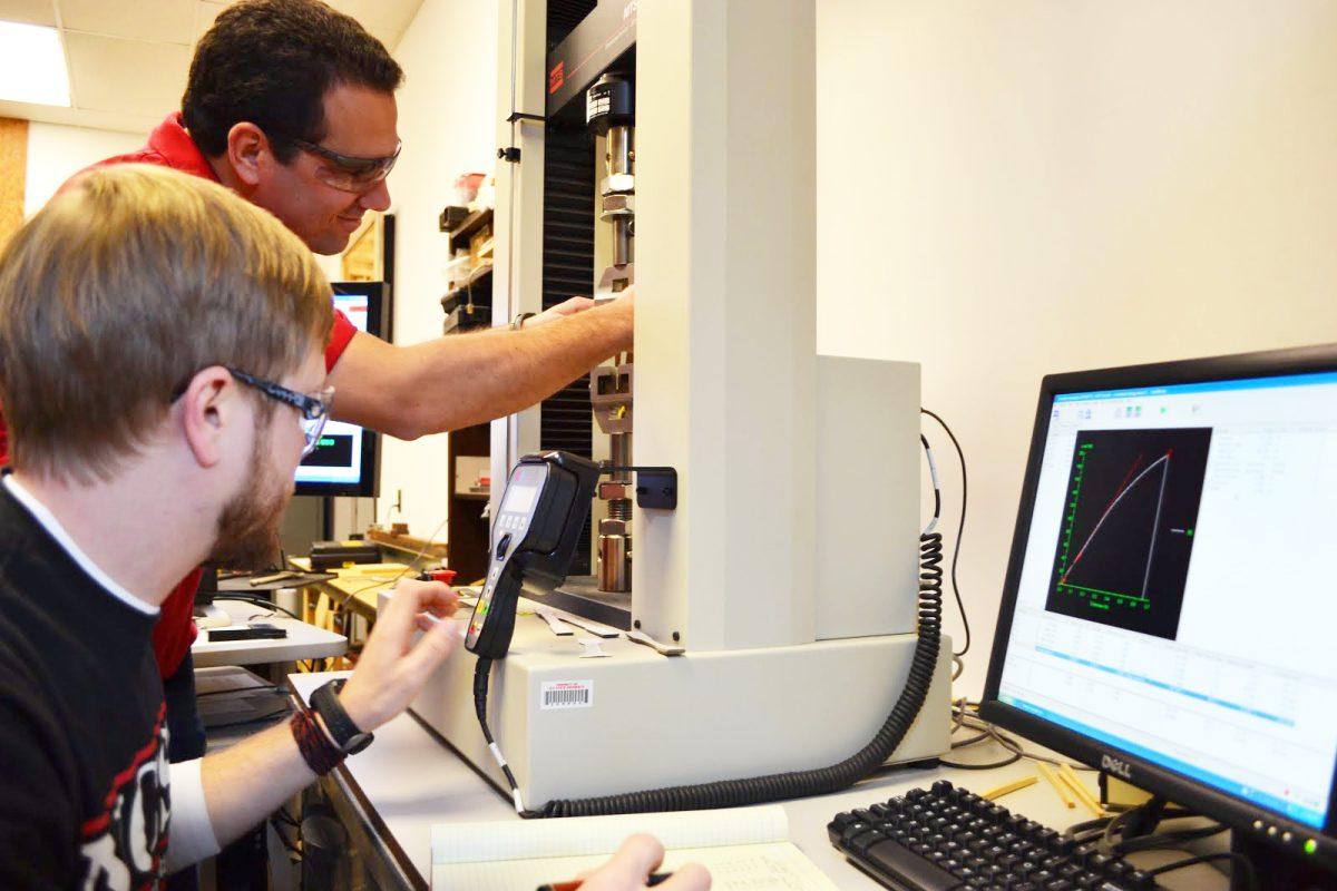Blake Hinton and Salim Taylor, both seniors in wood products, use a testing machine to evaluate the strength of solid wood to determine the effect of species or growth rates on the strength of the material.
