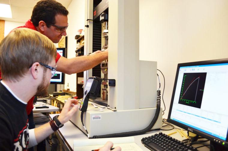 Blake Hinton and Salim Taylor, both seniors in wood products, use a testing machine to evaluate the strength of solid wood to determine the effect of species or growth rates on the strength of the material.