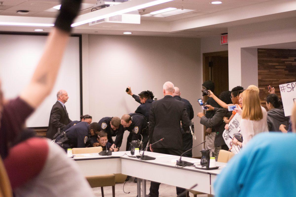 UNC-Chapel Hill student Madeleine Scanlon is forcibly removed from the Board of Governors meeting chamber during a protest. The protesters chanted, "When our system is under attack, stand up and fight back!"