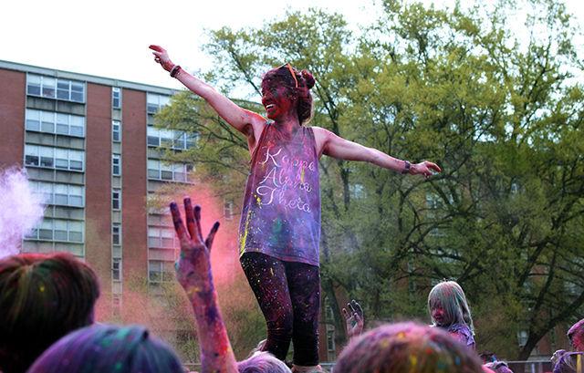 Sarah Take, a sophomore in design studies, stands on one of her friends and throws colors on the people around her. This took place on Saturday during Holi on Lee Field.