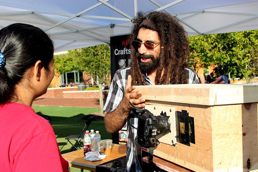 Fahad Alsuwaidi, a fourth-year studying nuclear engineering, explains the concept of a pinhole camera at NC State's Entrepalooza hosted at the Oval on Centennial Campus Thursday. NC State's Crafts Center was one of many booths at Entrepalooza, a festival celebrating entrepreneurs. Guests were able to have fun, play games and visit booths hosted by companies such as Smashing Boxes and Retrieving Hearts.&#160;