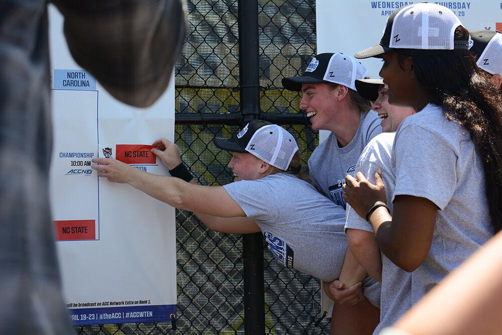 Junior Sophie Abrams places the NC State sticker in the champion slot on the bracket as she's lifted by junior Amelia Rajecki after the match against the University of North Carolina at Cary Tennis Park on Sunday, April 23, 2023. The Wolfpack defeated the Tar Heels 4-1.