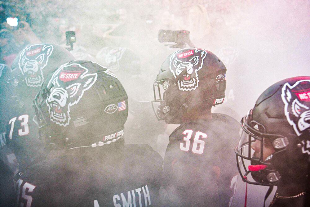 The Wolfpack heads out of the tunnel through smoke in their all black uniforms before the blackout night game against the Louisville Cardinals at Carter-Finley Stadium on Friday, Sept. 29, 2023. The Cardinals beat the Wolfpack 13-10.