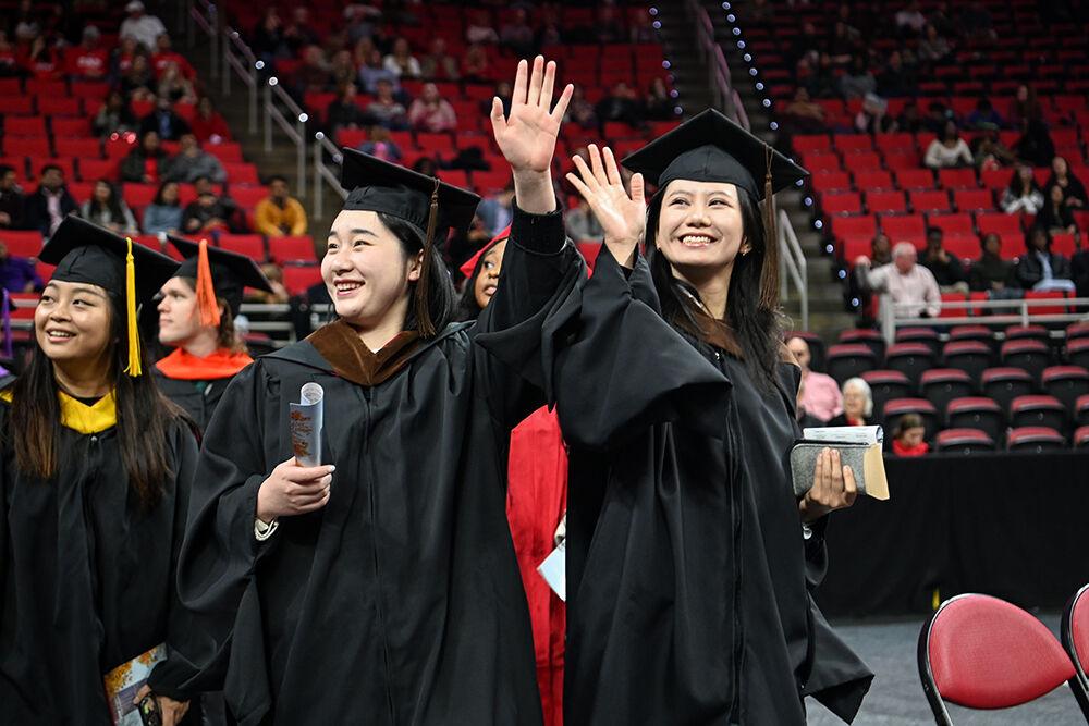 Yijing Li, a graduate student in landscape architecture, and Yuqi Su, a graduate student in landscape architecture, wave to their family while walking to their seats before the Fall Commencement Ceremony in PNC Arena on Saturday, Dec. 16, 2023. There were 3,282 graduates and 3,411 degrees were conferred during the ceremony.