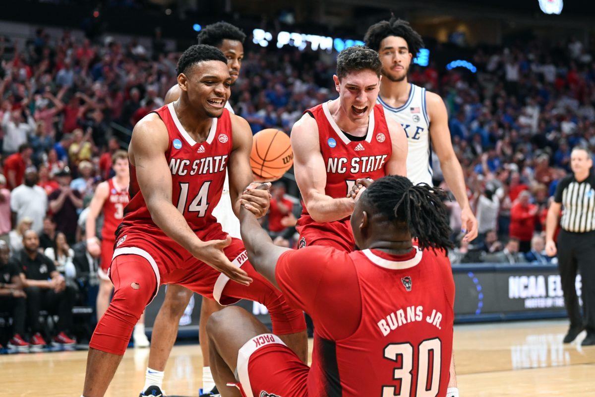 Graduate guards Casey Morsell and Michael O'Connell help graduate forward DJ Burns up after he scored an and-one layup during the NCAA Tournament Elite 8 game against Duke at American Airlines Center in Dallas on Sunday, March 31, 2024. Burns led in scoring with 29 points. NC State beat Duke 76-64 to advance to the Final Four.