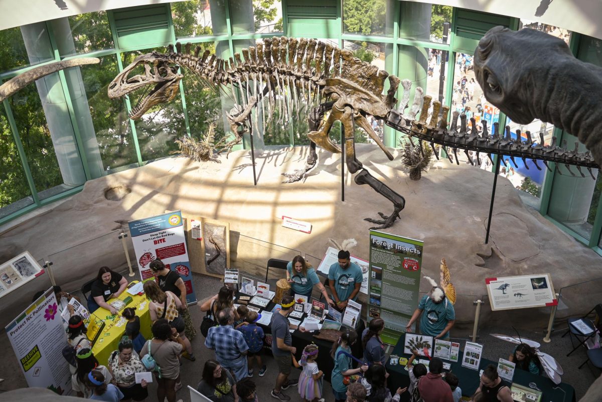 Booths in a room surrounded by dinosaur replicas and fossils during BugFest in Downtown Raleigh on Saturday, Sept. 20, 2025. Various booths were hosted during this event throughout the whole building and outside of the North Carolina Museum of Natural Sciences building.