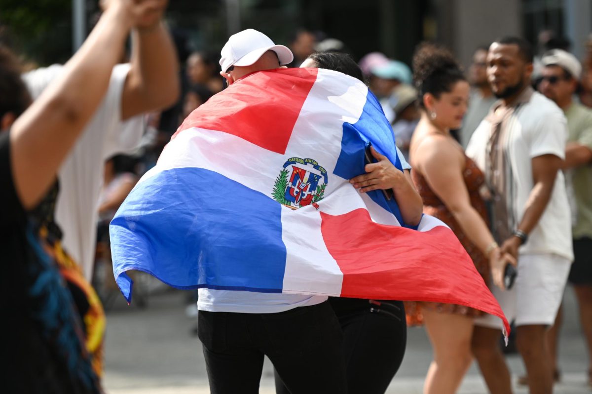 A Dominican Republic flag drapes across a festivalgoer’s back as he dances with a partner during La Fiesta del Pueblo at Fayetteville Street Historic District on Sunday, Sept. 21, 2025. The event, which draws thousands annually, is organized by El Pueblo to celebrate the pride and resilience of the Latine community.