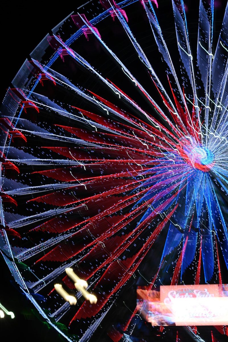 Lights from the Ferris Wheel light up the night sky during the North Carolina State Fair on Oct. 22, 2025. Visitors explore the fairgrounds filled with rides and food stands.