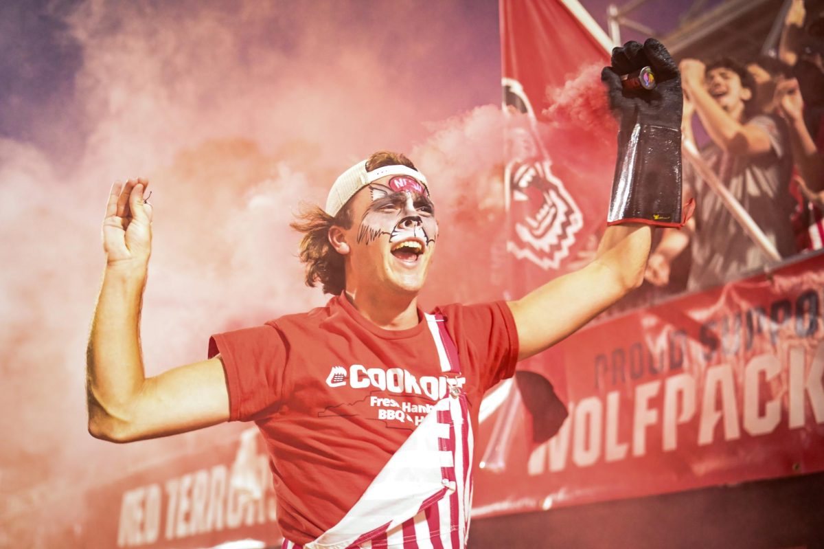 Andrew Smith, a first-year in industrial engineering, throws up "Wolfies" while waving around smoke after a goal during the game against Wake Forest in Dail Soccer Stadium on Thursday, Oct. 2, 2025. The Wolfpack defeated the Demon Deacons 2-1.