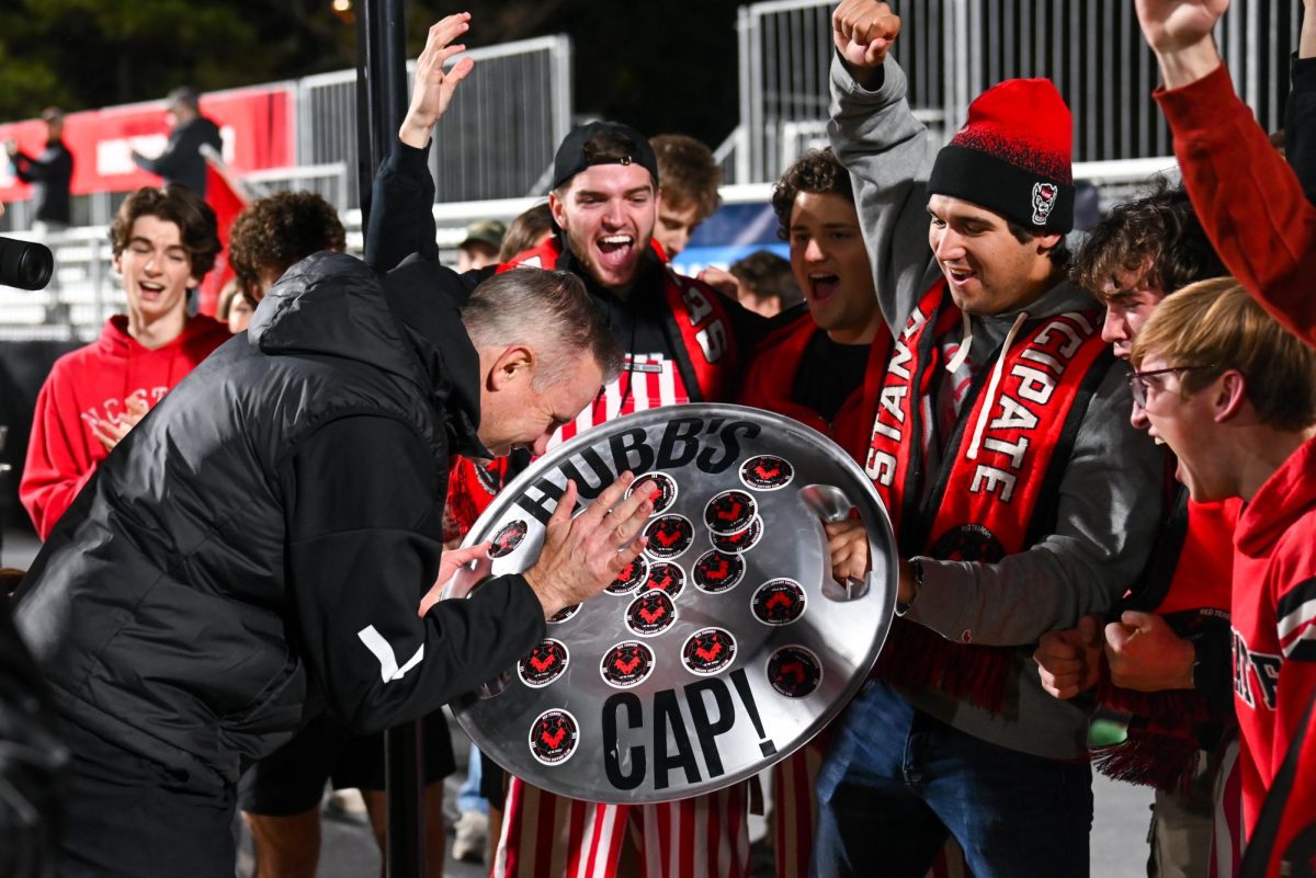 Head Coach Marc Hubbard slaps another sticker on “Hubb’s Cap” after the game against Marshall University at Dail Soccer Field on Sunday, Nov 23, 2025. “Hubb’s Cap” is a bottle cap with a sticker for each soccer game the Wolfpack played this season. NC State beat Marshall University 2-0.