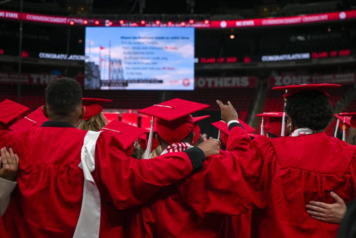 Newly graduated students join arms and sing NC State’s alma mater during the Fall Commencement Ceremony in the Lenovo Center on Saturday, Dec. 13, 2025. During the ceremony, graduates from all academic colleges including Engineering, Humanities and Social Sciences, Design and Agriculture and Life Sciences were recognized for their achievements.