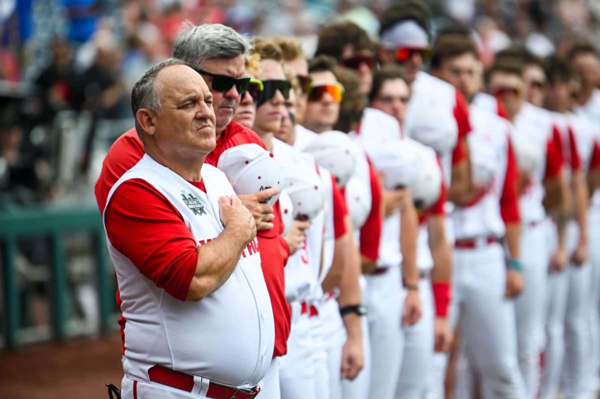 Head coach Elliott Avent stands with the NC State team for the national anthem before the Wolfpack's Men's College World Series game against the Florida Gators on Charles Schwab Field in Omaha, Nebraska, on Monday, June 17, 2024.