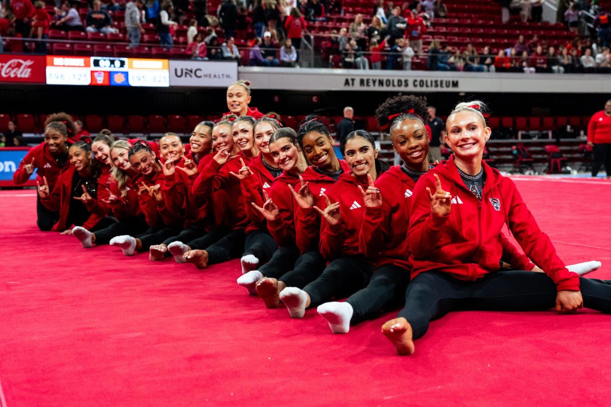 NC State gymnasts put up the "wolfies" hand sign for a photo after the meet against Clemson in Reynolds Coliseum on Saturday, Jan. 17, 2026. The Wolfpack defeated the Tigers 196.125-195.925.