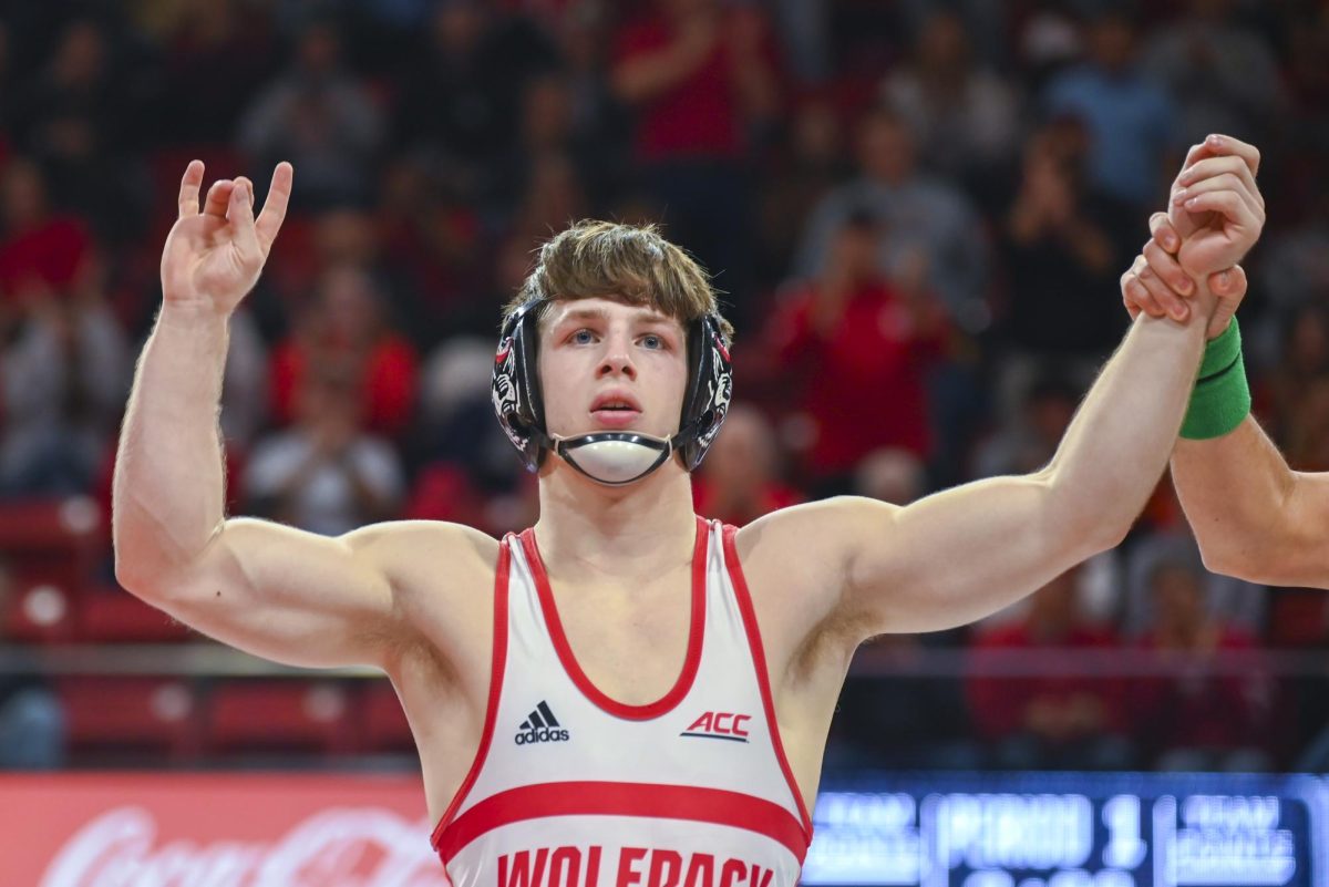 Redshirt sophomore Koy Buesgens holds up a "wolfie" during the wrestling match against Virginia in Reynolds Coliseum on Friday, Jan. 9, 2026. Buesgens won the 149 bout 4-2, putting NC State on the scoreboard for the first time that night in the process. NC State beat Virginia 19-17.