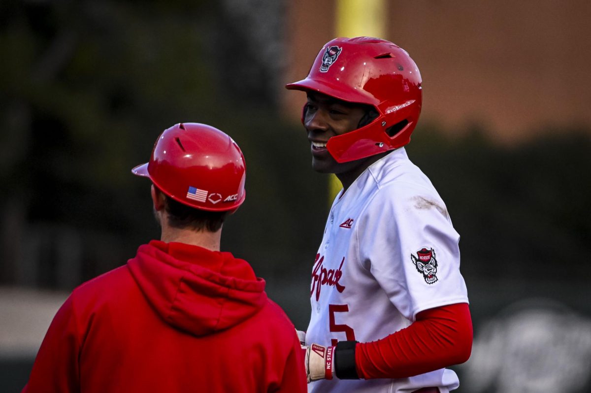 Junior infielder Sherman Johnson laughs with the first-base coach during the game against Richmond at Doak Field in Dail Park on Tuesday, Feb. 24, 2026. Johnson recorded two RBIs. The Wolfpack defeated the Spiders 27-0.