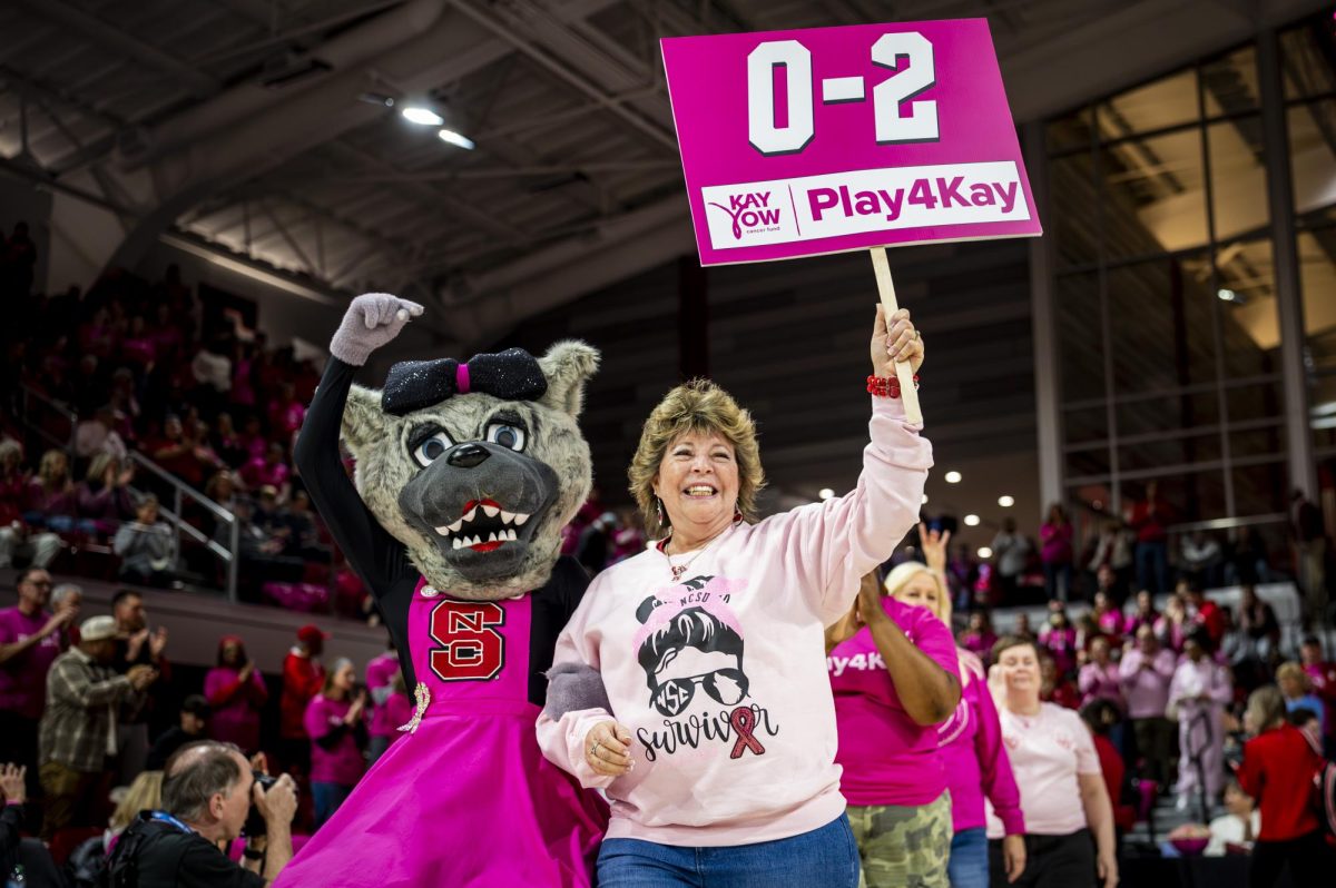 One-year cancer survivor Jennifer Day, speaker for the group of 0-2 year survivors, walks onto the floor with Ms. Wuf during halftime of the Play4Kay game against UNC in Reynolds Coliseum on Monday, Feb. 2, 2026. The halftime celebration commemorated the vision of coach Kay Yow in uniting players, coaches, officials and fans to fundraise for cancer research.