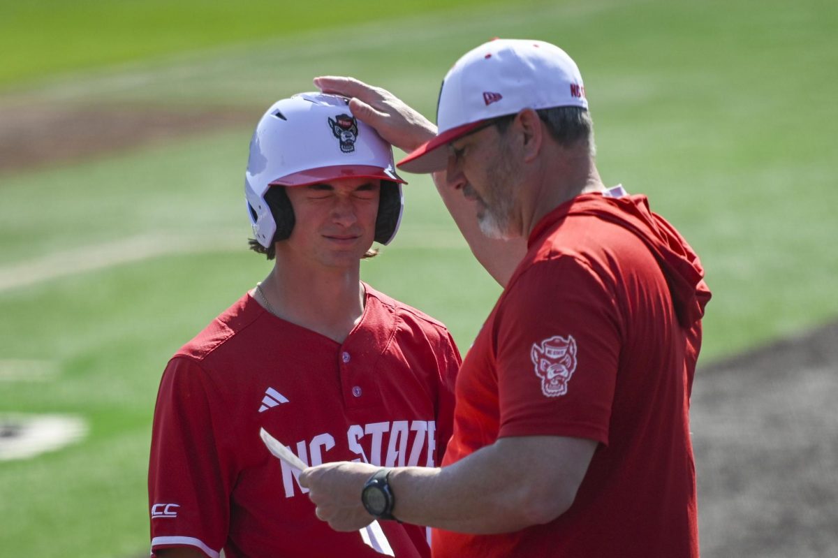 Freshman outfielder Rett Johnson gets patted on the helmet by assistant coach Bo Robinson during the game against Sacred Heart in Doak Field in Dail Park on Sunday, March 1, 2026. The Wolfpack defeated the Pioneers 13-0.