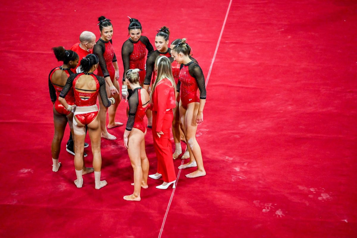 The team meets with their coaches on the floor during the meet against West Virginia at Reynolds Coliseum on Friday, March 13, 2026. The Wolfpack defeated the Mountaineers by a score of 196.650 to 195.725. 