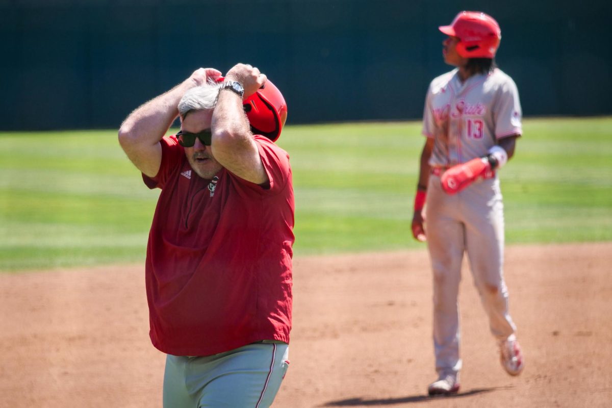 Third base coach Chris Hart holds his helmet above his head in disbelief after junior outfielder Andrew Wiggins collides with a ground ball, recording an out during the game against Stanford at Klein Field at Sunken Diamond on Sunday, May 10, 2026. The Cardinal defeated the Wolfpack by a score of 9-5.