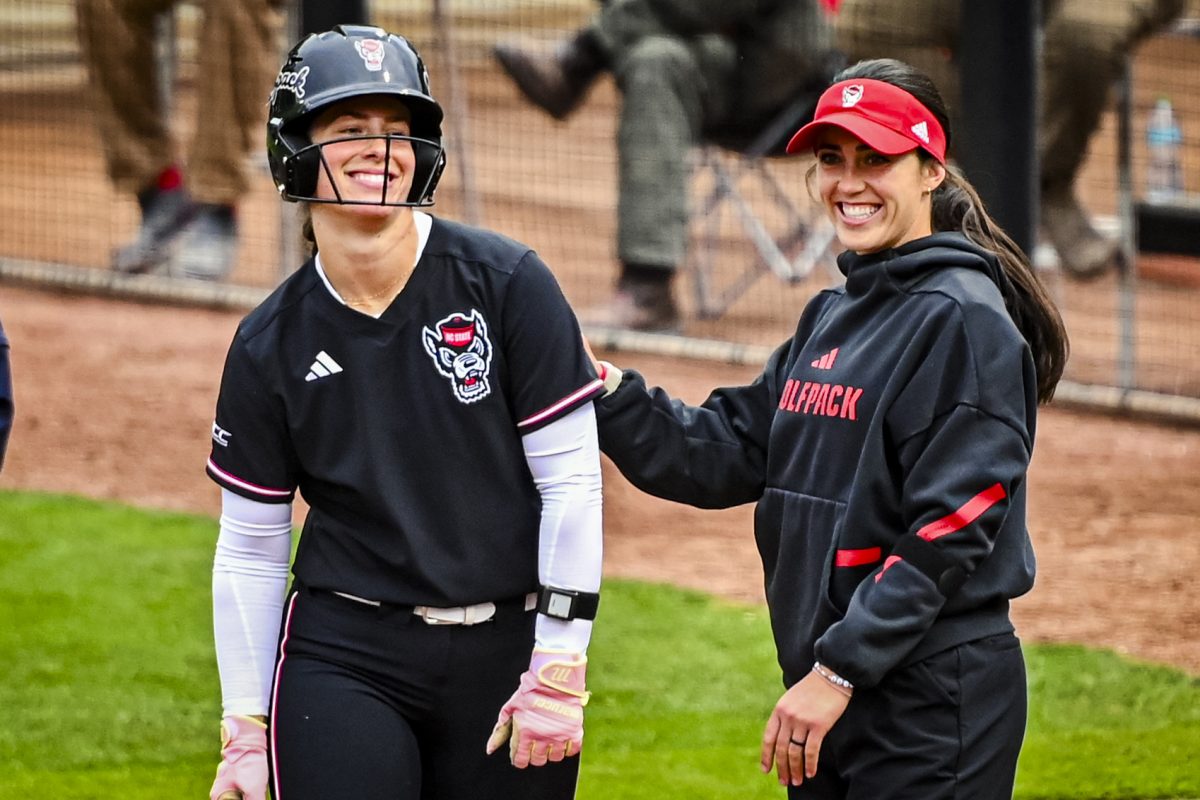 Senior catcher Ellington Whitaker smiles with assistant coach Grayson Radcliffe on first during the game against Louisville at Dail Softball Stadium on Saturday, May 2, 2026. NC State defeated Louisville 10-6.